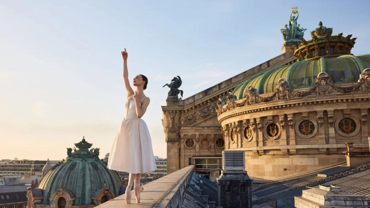 Étoile dancer Bleuenn Battistoni poses en pointe on the rooftop of the Palais Garnier, with the ornate green copper domes of the Paris Opera House rising behind her against a clear sky