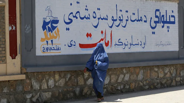 Une femme passe devant un panneau célébrant les 5 ans du retour des Talibans au pouvoir
