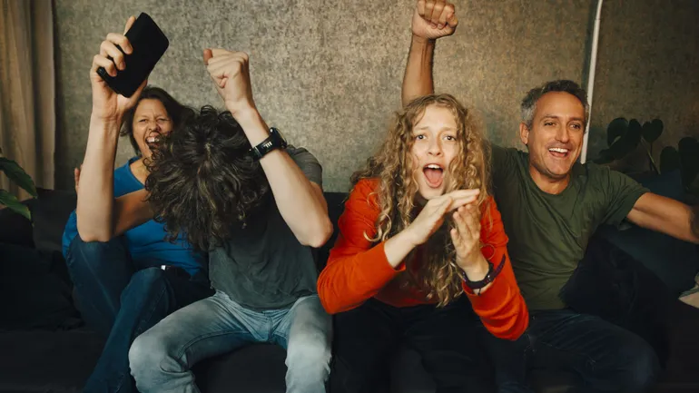 Happy parents with children cheering while watching sports in living room at night